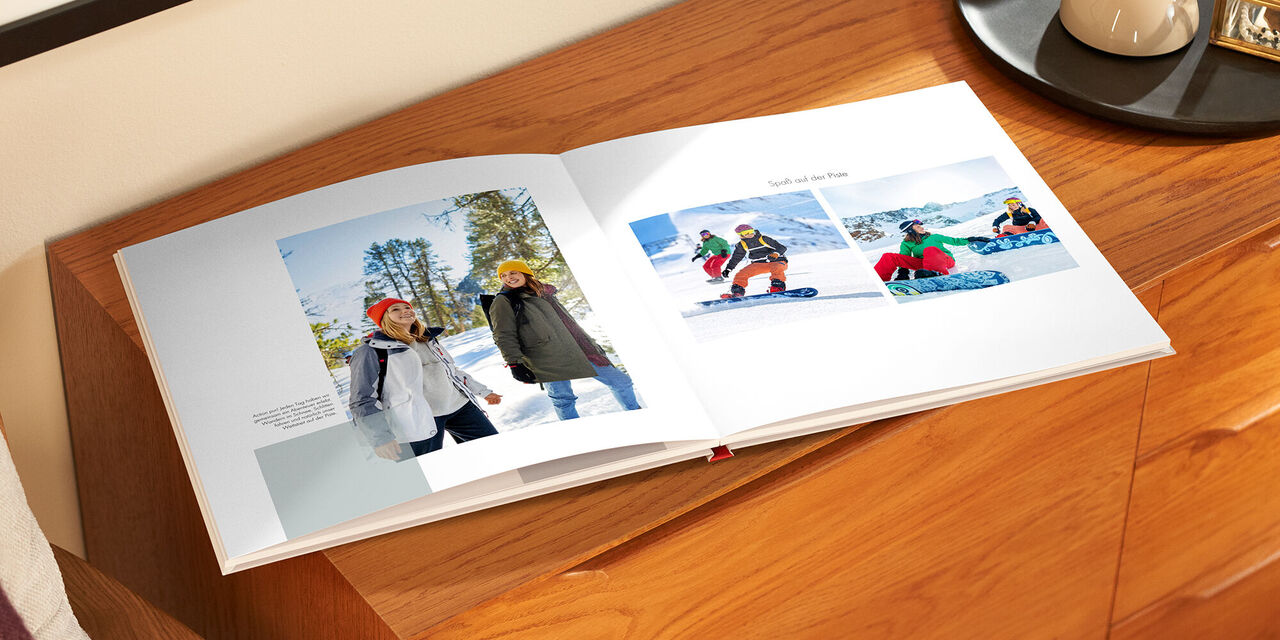 Il fotolibro aperto è appoggiato su un mobile di legno. A sinistra c’è la foto di due donne che fanno una gita. Accanto c’è un piccolo testo. Sul lato destro ci sono due foto di donne che fanno snowboard. Sopra di esse c’è la didascalia «Divertimento sulle piste».