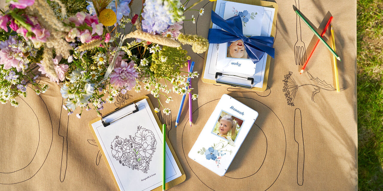 Su un tavolo ci sono matite colorate in una scatola di metallo con un design floreale, la foto di un bambino e un’immagine da colorare.